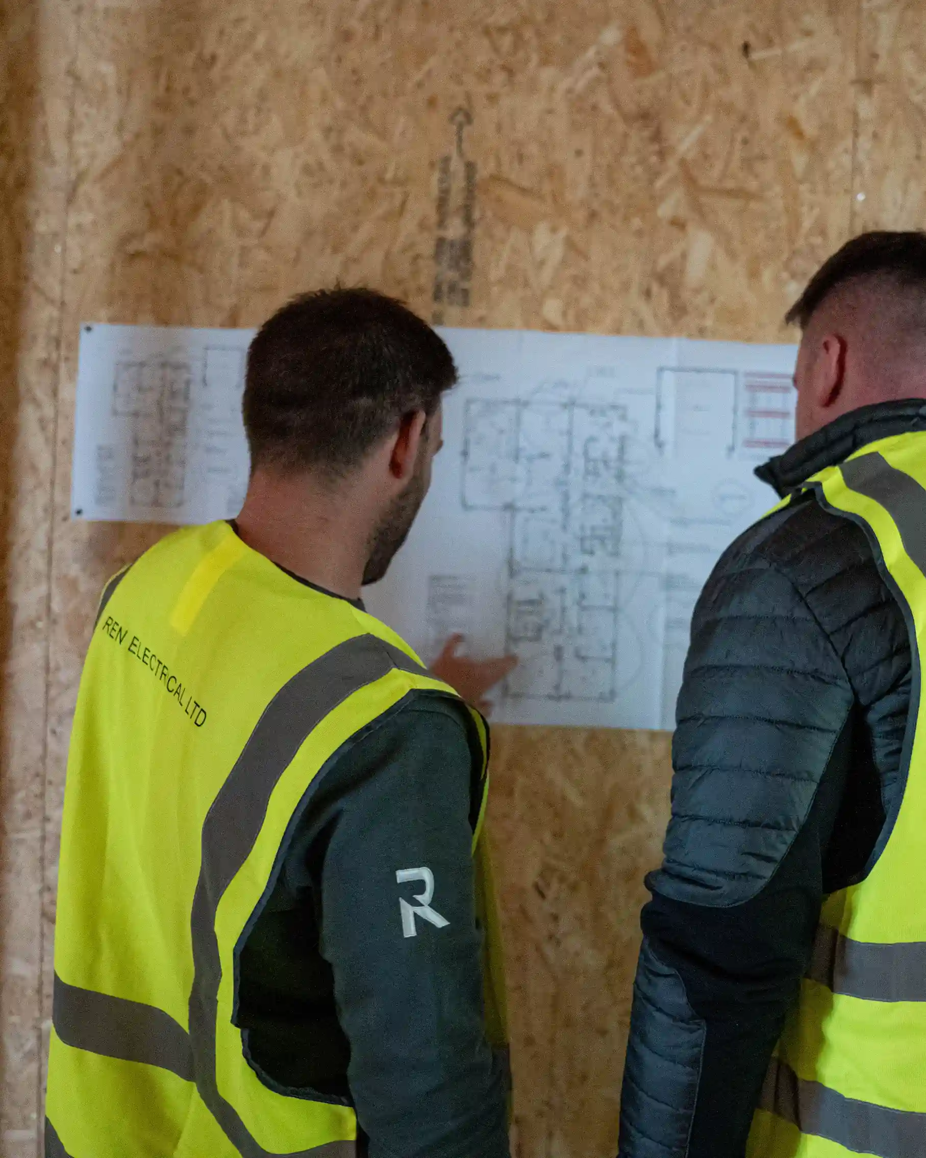 Ren Electrical team in hi-vis vests reviewing site plans on OSB wall - Ren Contractors commercial construction, Cornwall.