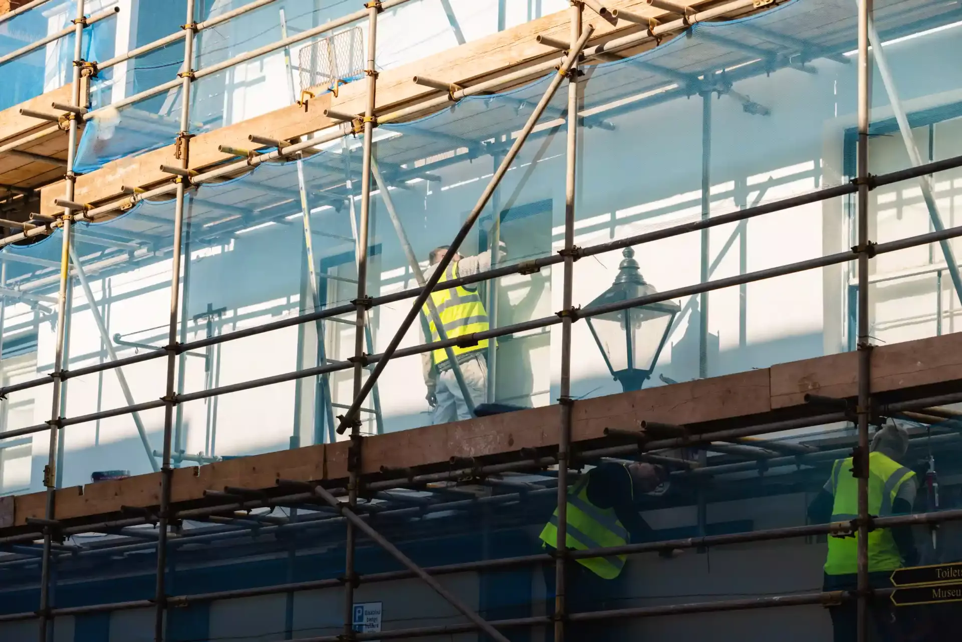 Scaffolded commercial building facade with workers in hi-vis vests during building renovation – Ren Contractors & Ren Electri