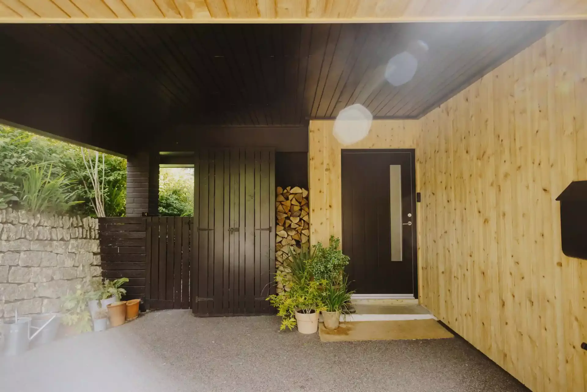 Primrose Cottage covered entrance with timber cladding, black door and stacked logs — Ren Contractors, Cornwall building reno